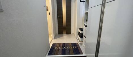 A narrow hallway with a welcome mat, a door at the end, and a white cabinet on the right.