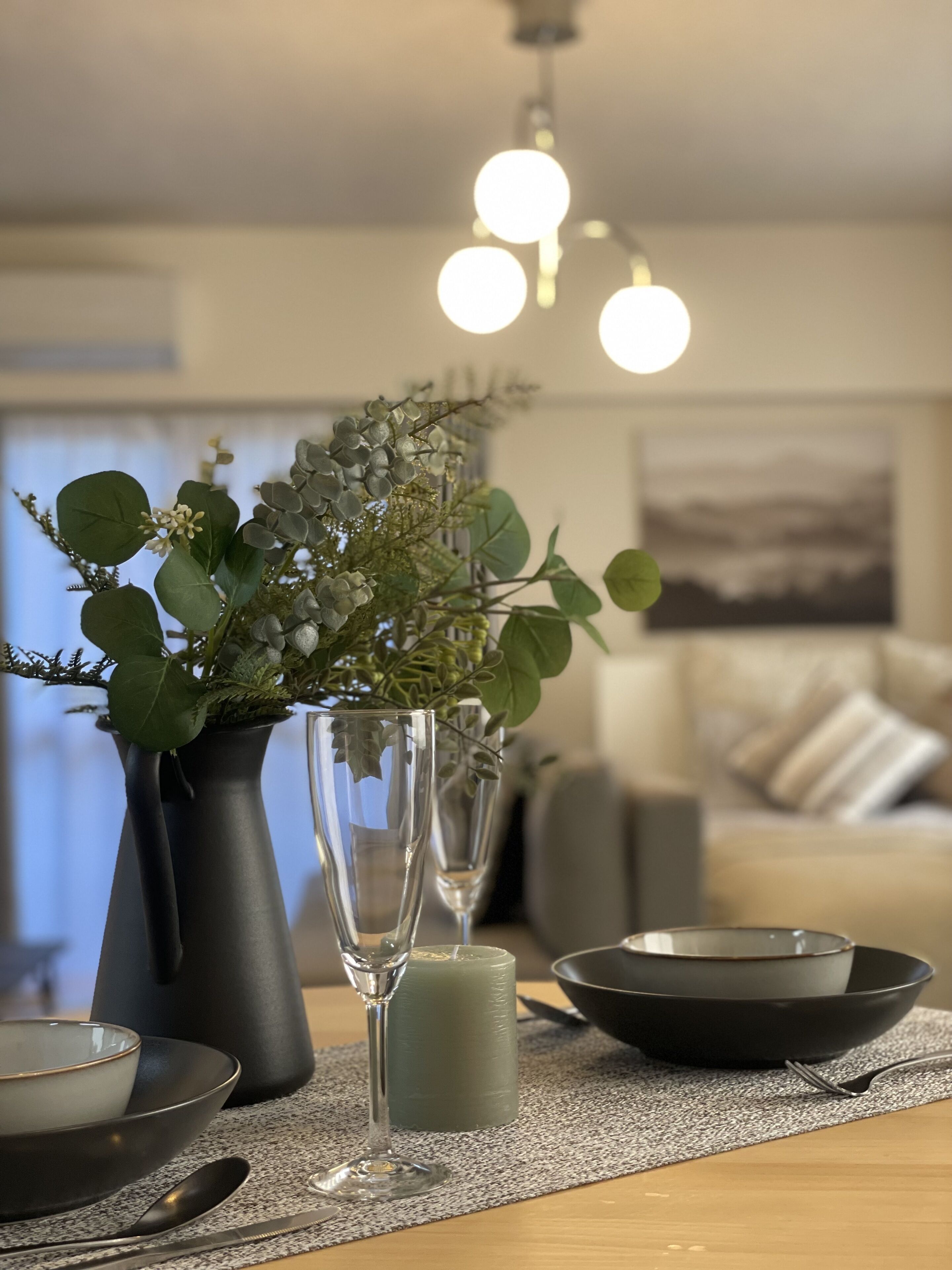 Una mesa de comedor con un florero de follaje, una vela y un vaso.