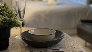 A neatly arranged dining area with a table set for two, a glass of water, and a bowl. A bed with a white comforter and pillows is visible in the background. - Oak Stay Shimokitazawa  (Tokyo)