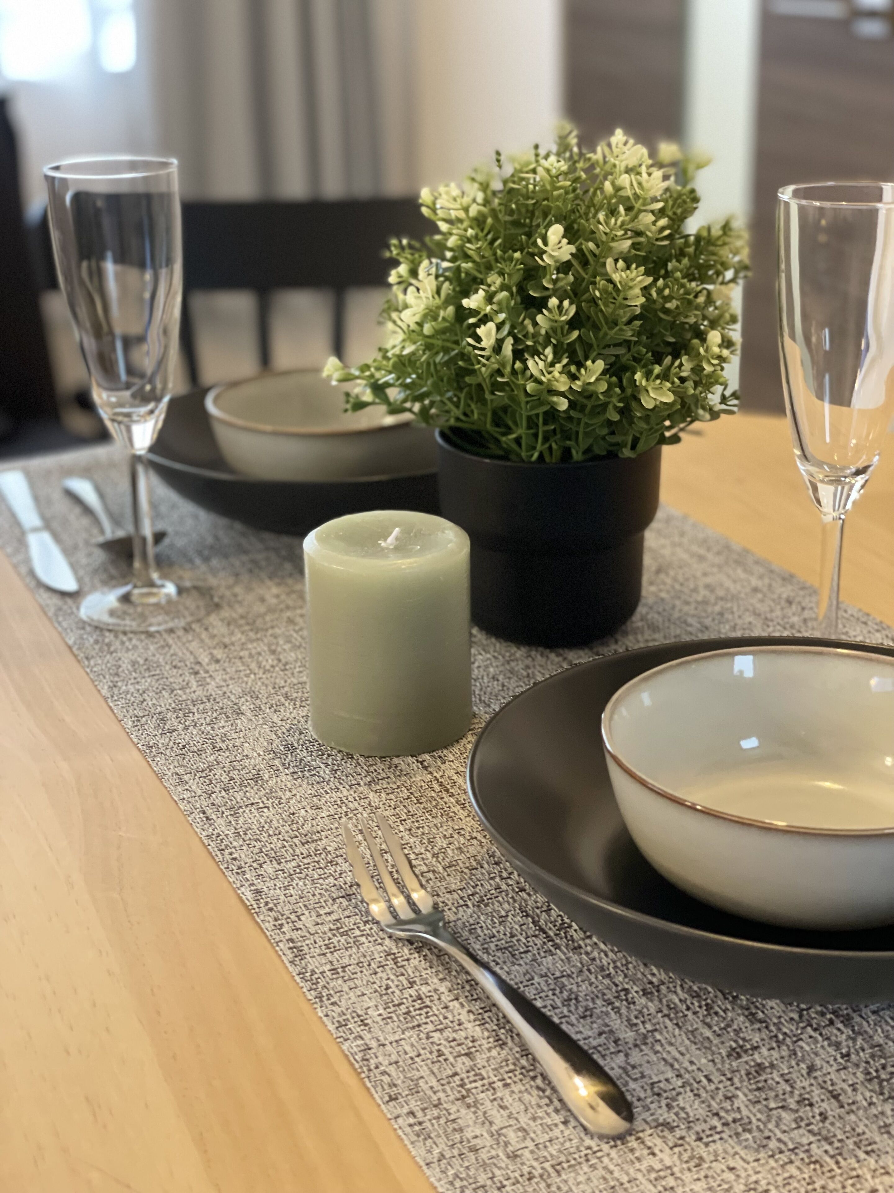 A dining table set with a candle, a potted plant, and two glasses.