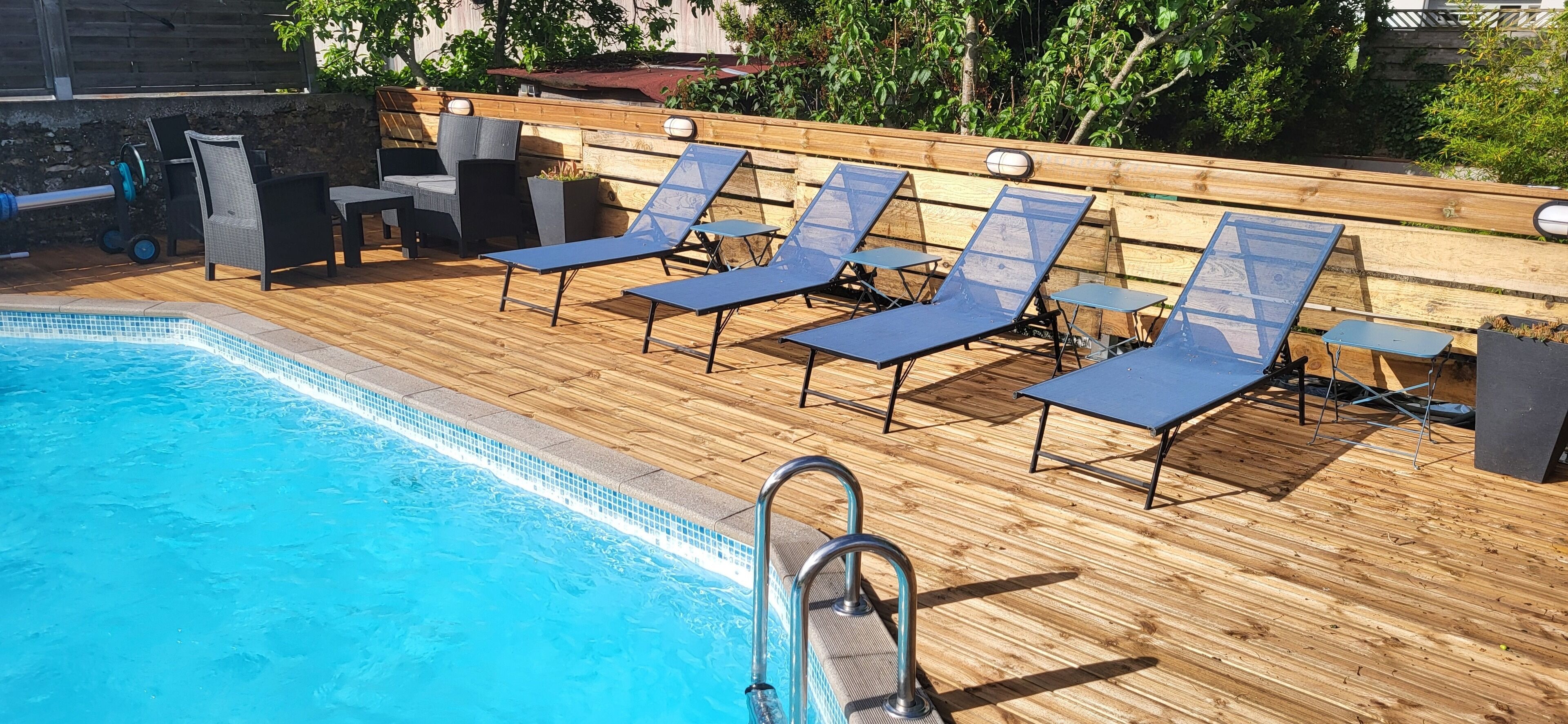 A poolside area with a wooden deck, lounge chairs, and a pool.