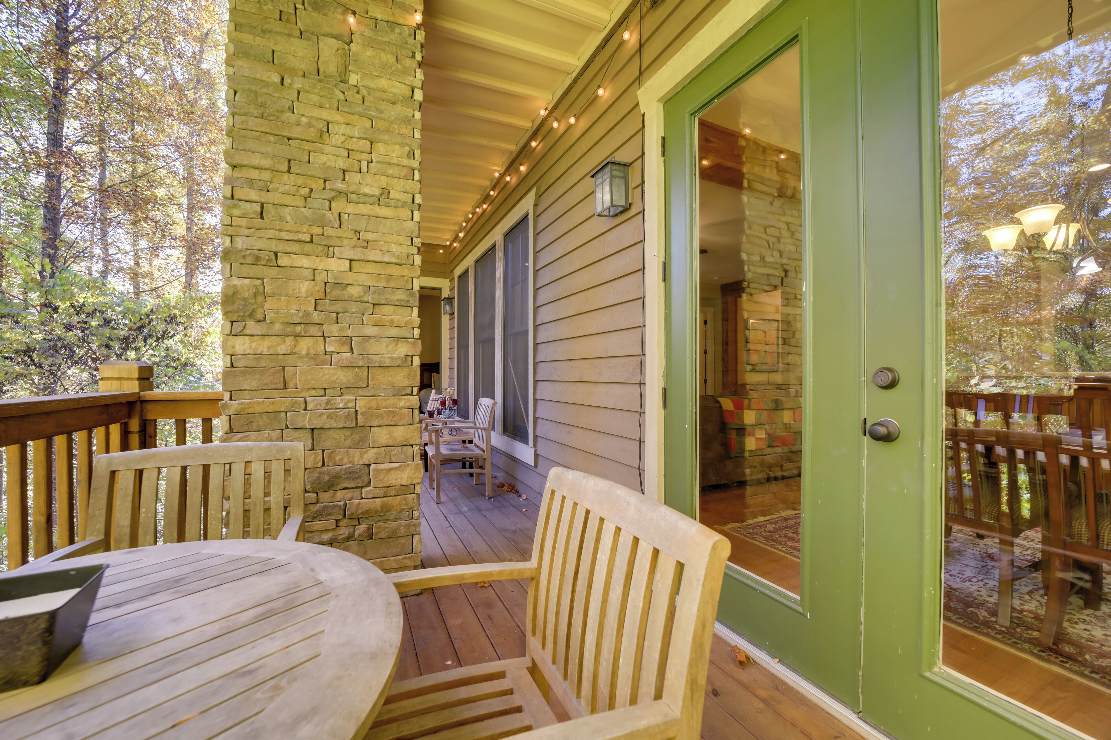 Une terrasse en bois avec une table et des chaises, un pilier en pierre et une porte verte donnant sur un espace intérieur.