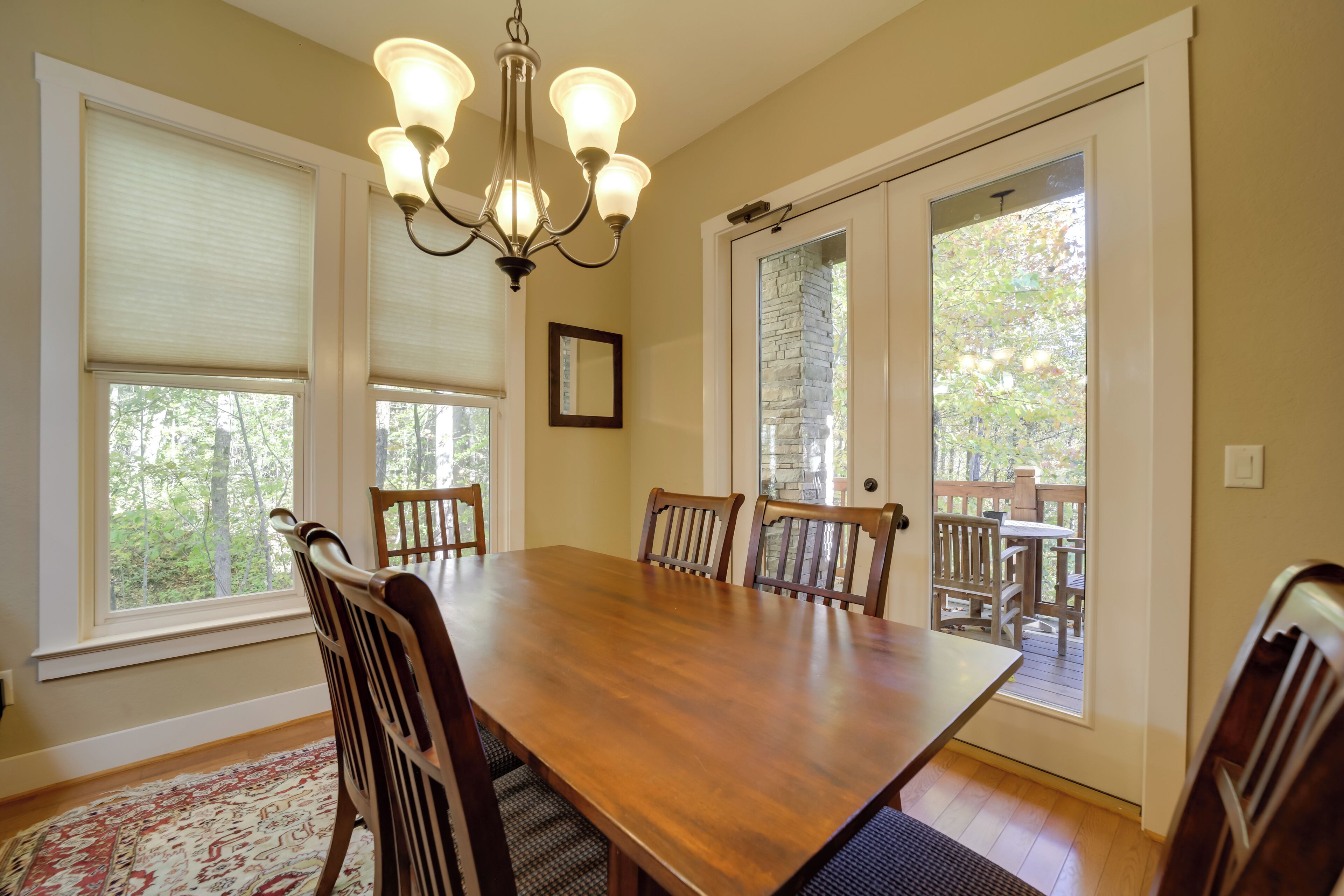 Comedor con mesa y sillas de madera, ventanas amplias, una lámpara de araña y vistas al exterior.