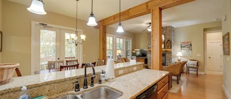 Una cocina con encimeras de granito, pileta de acero inoxidable, gabinetes de madera e iluminación colgante.