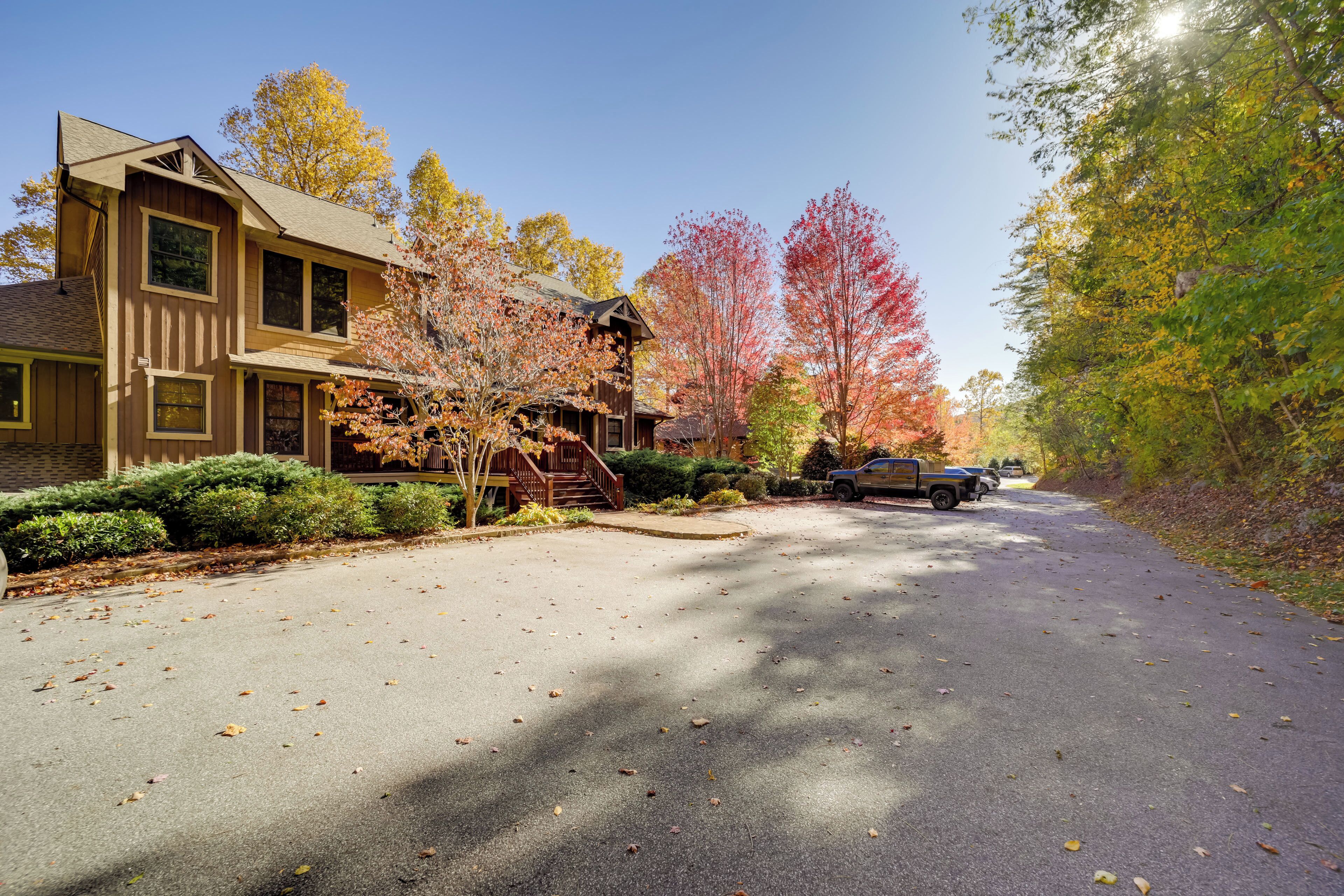 A two-story house with a front porch, a driveway, and autumn-colored trees.