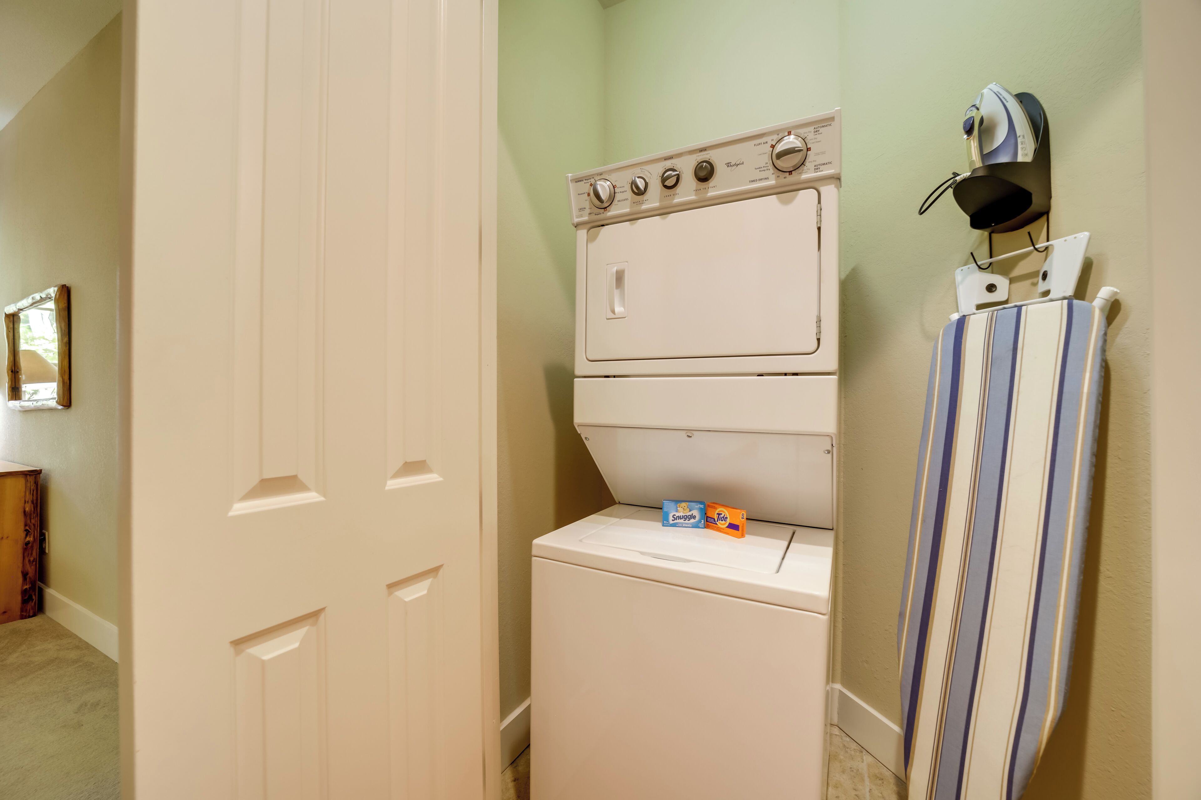 A laundry area with a stacked washer and dryer, a striped towel hanging on a rack, and a wooden cabinet in the background.