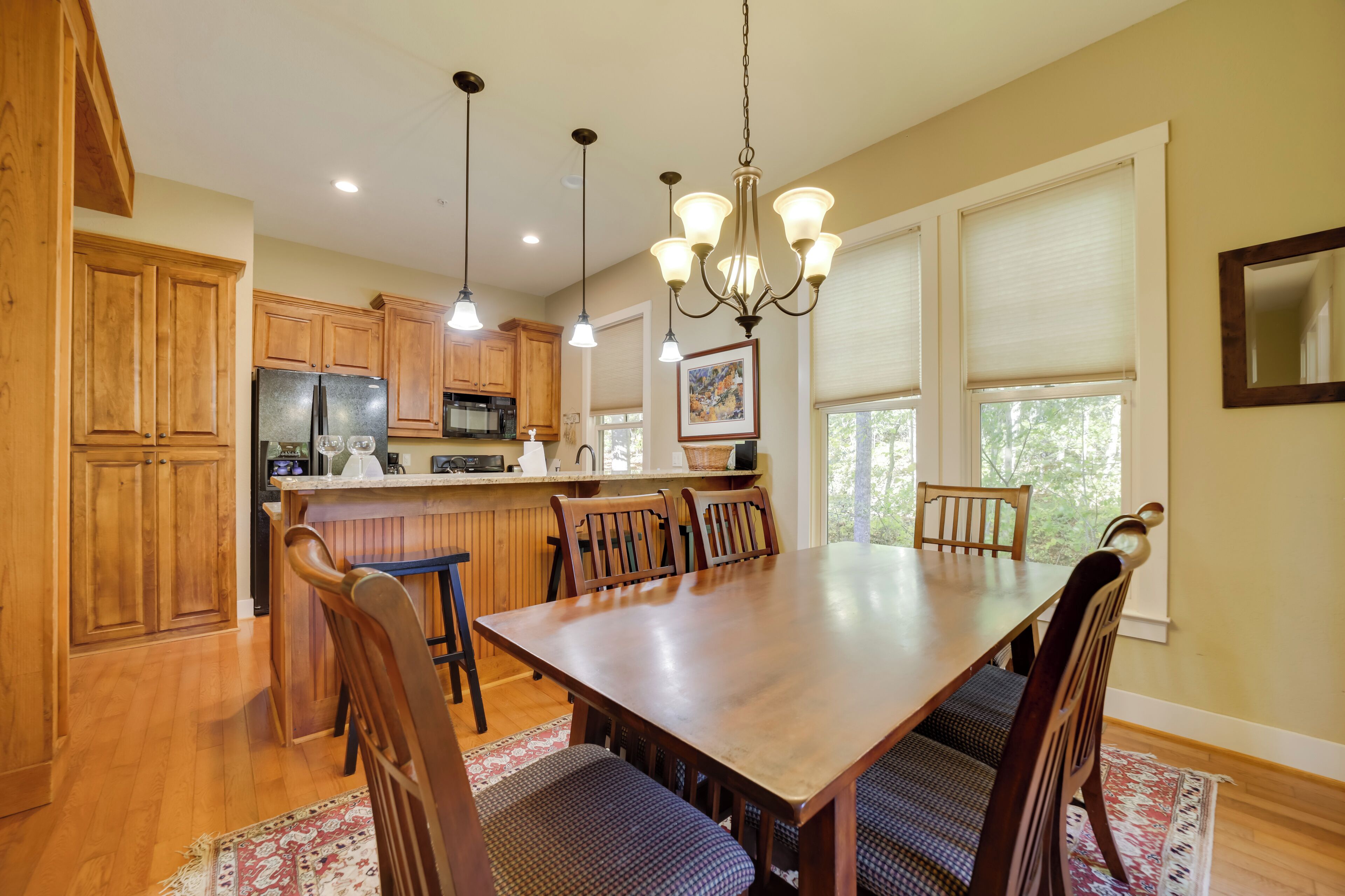 A spacious dining area with a large wooden table and chairs, wooden cabinets, and a kitchen in the background.