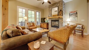 A cozy living room with a stone fireplace, a ceiling fan, and a large window. - Condo w/ Pool & Beach Access in Bear Lake Reserve! (Tuckasegee)