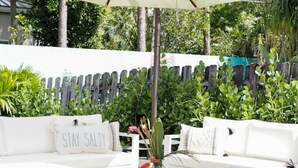Ein Außenbereich mit weißen Sofas, einem Holztisch und einem großen Sonnenschirm.