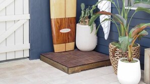 Eine duschrückwand aus Holz im Surfbrett-Design an einer dunkelblauen Wand, mit einer weißen Tür und einer kleinen Holzplattform davor.