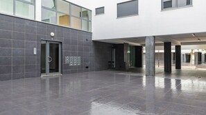 Ein modernes Gebäude mit nasser Bodenfläche, was auf kürzlichen Regen hindeutet. Es gibt zwei Türen mit Glasfeldern, wobei eine Tür mit der Nummer 12 gekennzeichnet ist.
