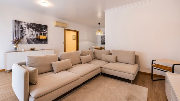 Ein modernes Wohnzimmer mit einem beigefarbenen Ecksofa, einem kleinen Tisch und einer Wand-Klimaanlage.