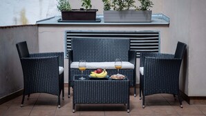 A balcony with wicker furniture, a table with fruit and drinks, and potted plants.