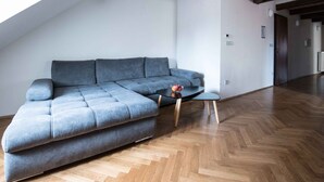 A modern living room with a grey sectional sofa, a small black table, and a herringbone wooden floor.