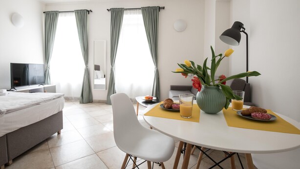 A hotel room with a bed, a TV, a dining table with breakfast items, and a vase with flowers.