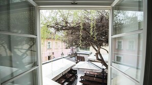 A view through a window of a courtyard with outdoor seating, a tree, and buildings in the background.