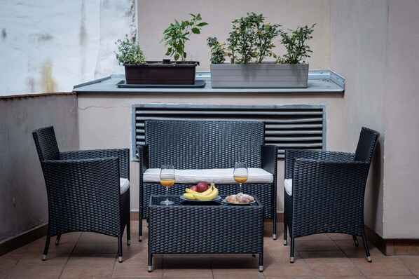 A balcony with wicker furniture, a table with fruit and drinks, and potted plants.