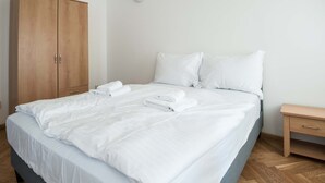 Een netjes opgemaakt bed met witte lakens en handdoeken, een houten garderobe en een klein nachtkastje.