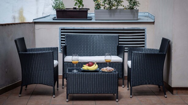 Een balkon met rieten meubels, een tafel met fruit en drankjes, en potplanten.