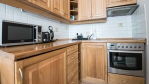 Een keuken met houten kastjes, een magnetron, een koffiezetapparaat en een oven.