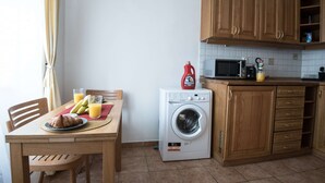 Een compacte keuken met houten kastjes, een wasmachine, een magnetron en een ontbijthoek met ontbijtartikelen.