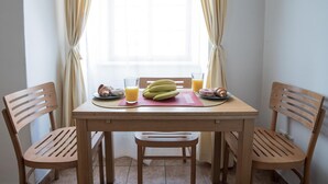 Een houten eettafel met een placemat, twee stoelen, een bord met bananen, een glas sinaasappelsap en een croissant.