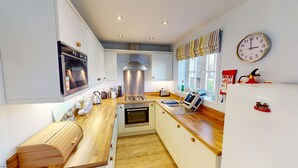 A modern kitchen with white cabinets, stainless steel appliances, a wooden countertop, and a window with a view. - Stunning 2 bed coastal cottage - Pool and Beach Access Included. (Filey)