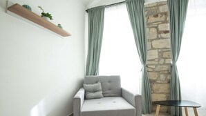 En moderne stue med en grå sofa, et lille bord, en træreol med planter og en stenvæg.