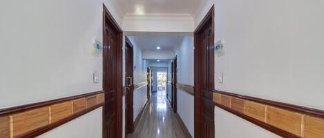 Un pasillo largo y estrecho con puertas de madera y suelo de baldosas.
