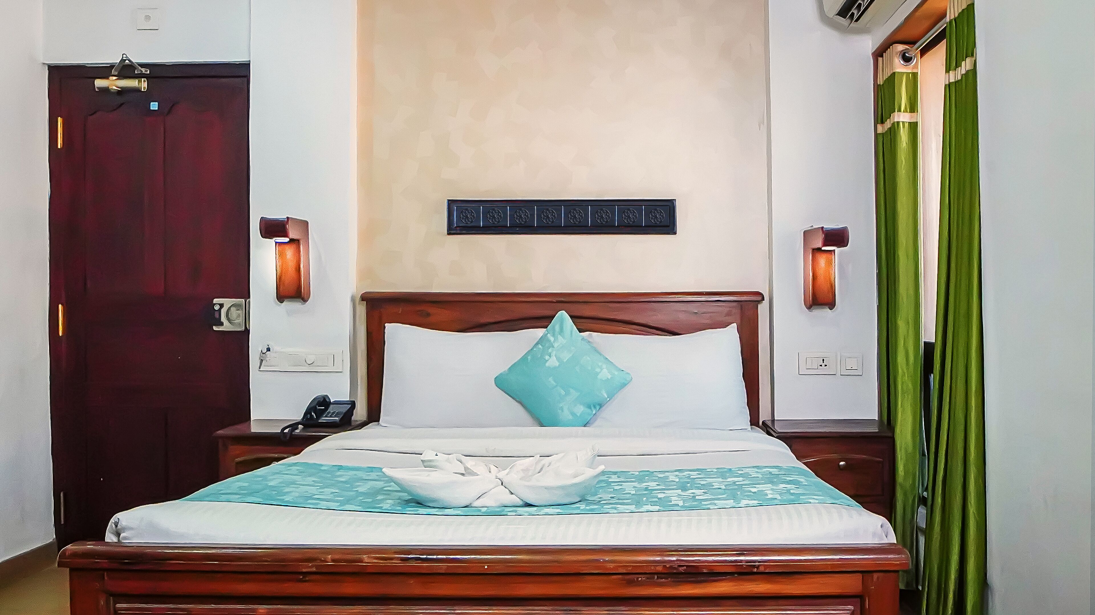 A neatly made bed with a wooden headboard, a bedside phone, and a wall-mounted light fixture.