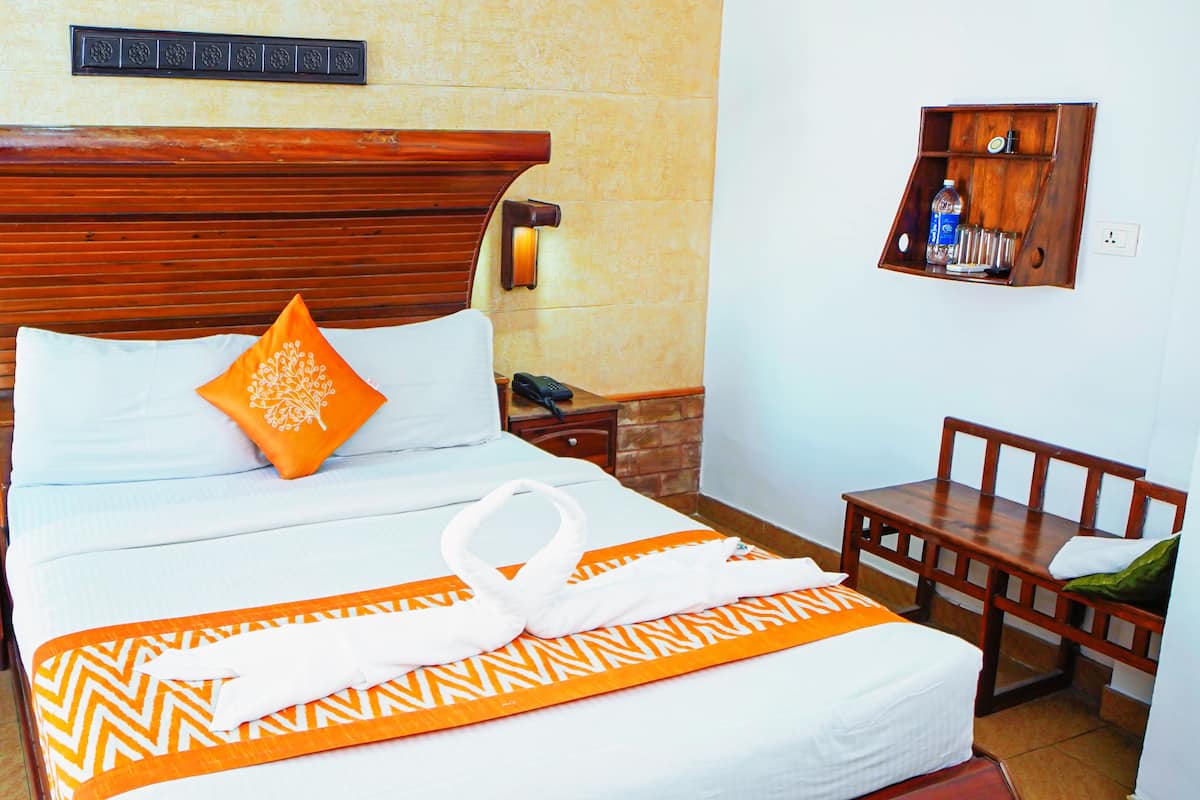 A neatly made bed with a wooden headboard, a bedside table with a kettle, and a small wooden side table with a phone.