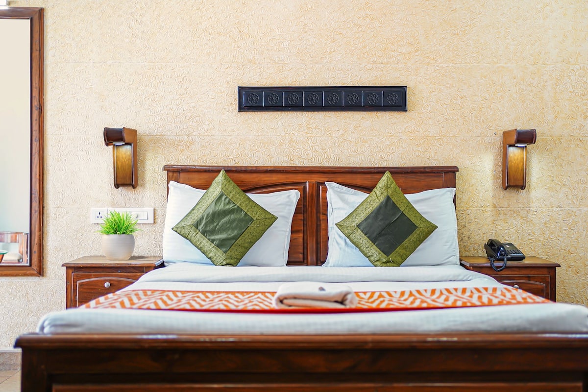 A neatly made bed with a wooden headboard, two decorative pillows, a bedside table with a lamp, and a wall-mounted phone.