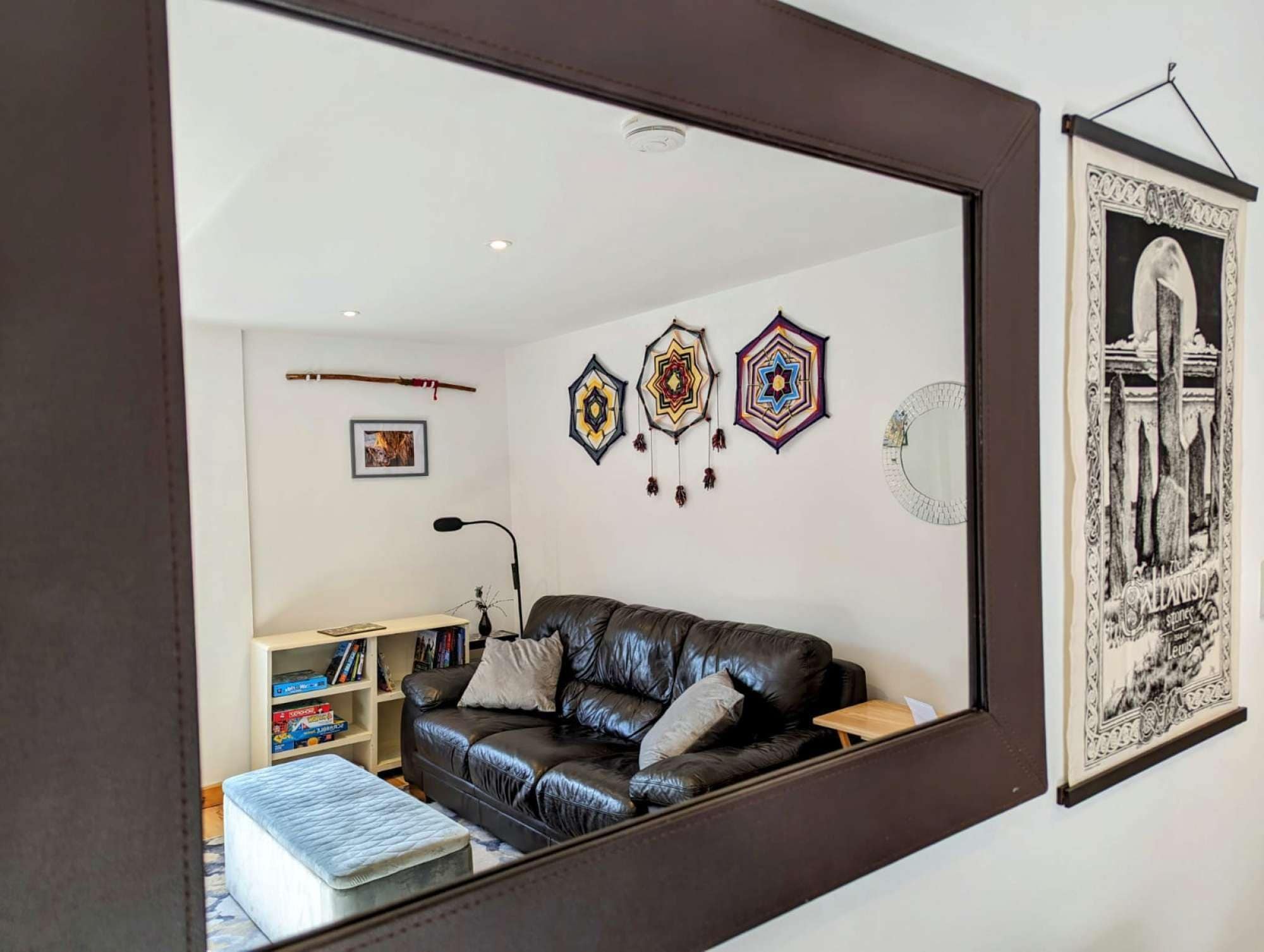 Een woonkamer met een zwarte leren bank, een boekenkast en decoratieve muurkunst.