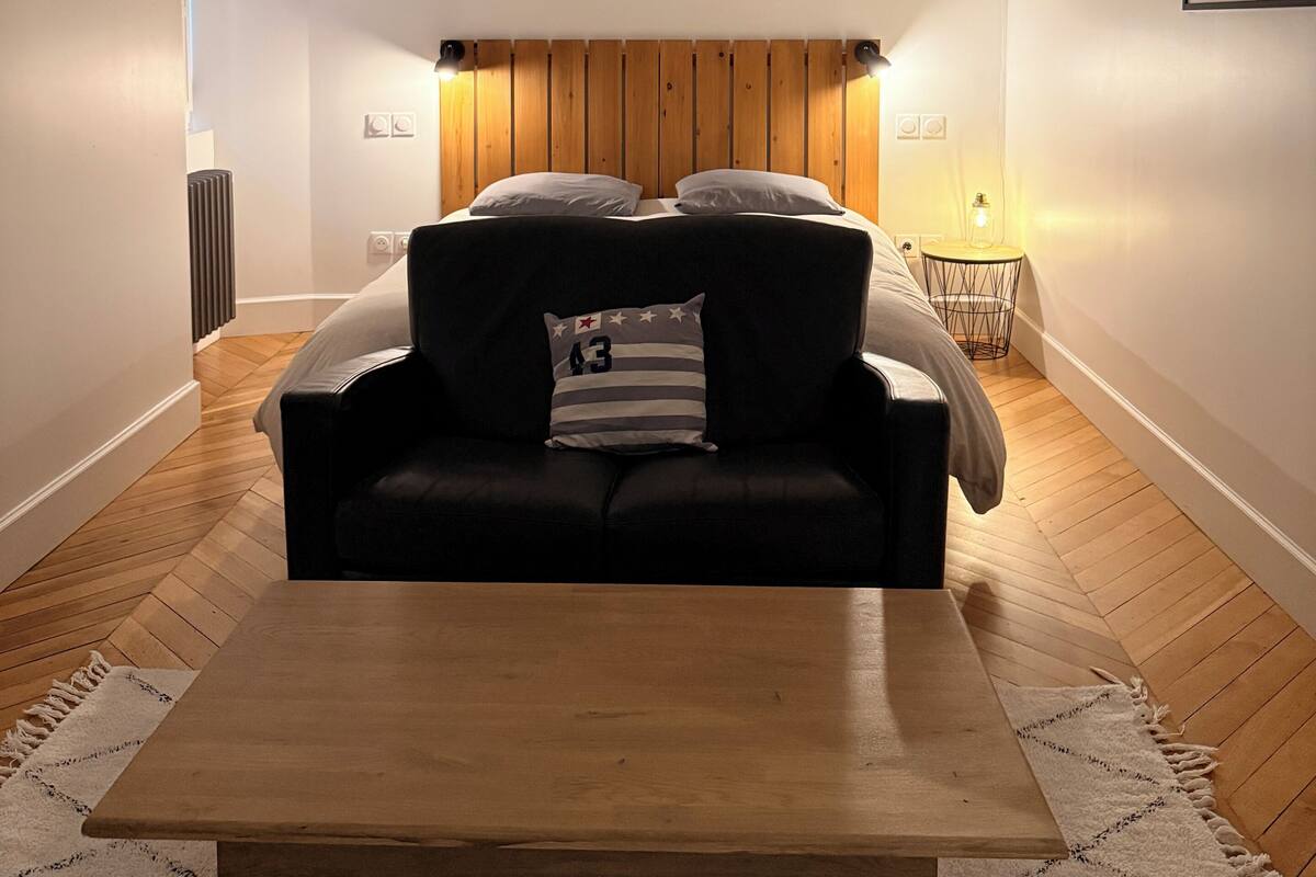 Een moderne woonkamer met een bank, een houten salontafel en een houten hoofdbord. Er hangen ingelijste foto's aan de muur en in de achtergrond staat een radiator.