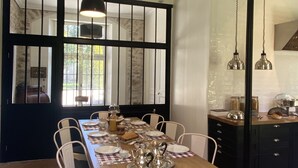 Un comedor con una mesa de madera dispuesta para seis personas, sillas blancas y una lámpara colgante negra.