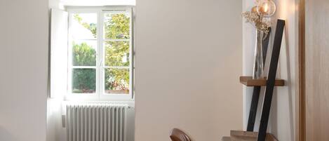 A bedroom with a bed, a chair, a radiator, a window, and a wall-mounted shelf with a vase.