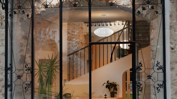Un interior moderno con un separador de vidrio, una escalera y un comedor con una mesa y sillas blancas.