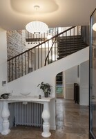 Uma escada com corrimão branco, uma mesa branca com uma planta e um radiador.