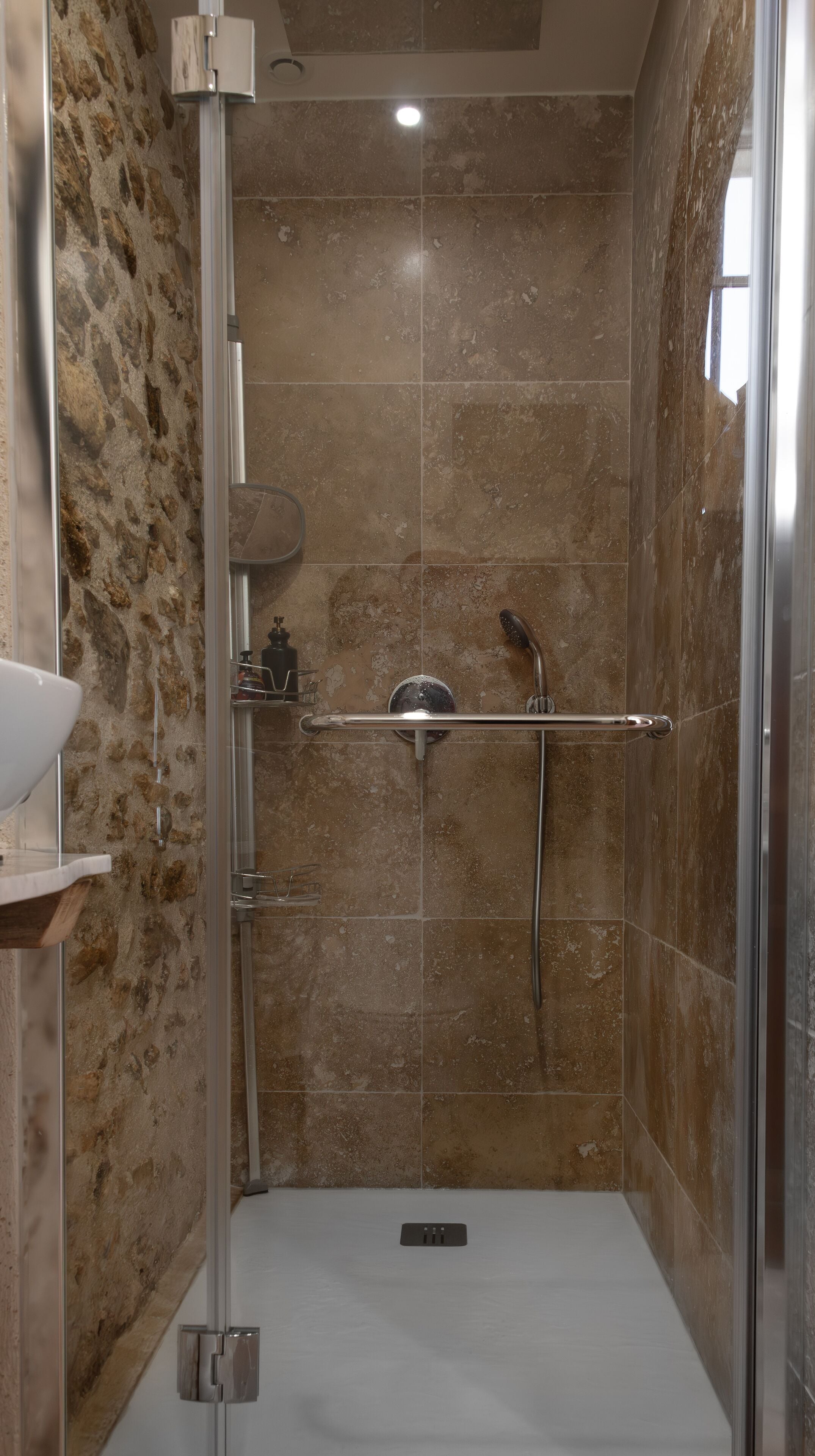 A modern shower with a glass door, a handheld showerhead, and a handheld shower bar.