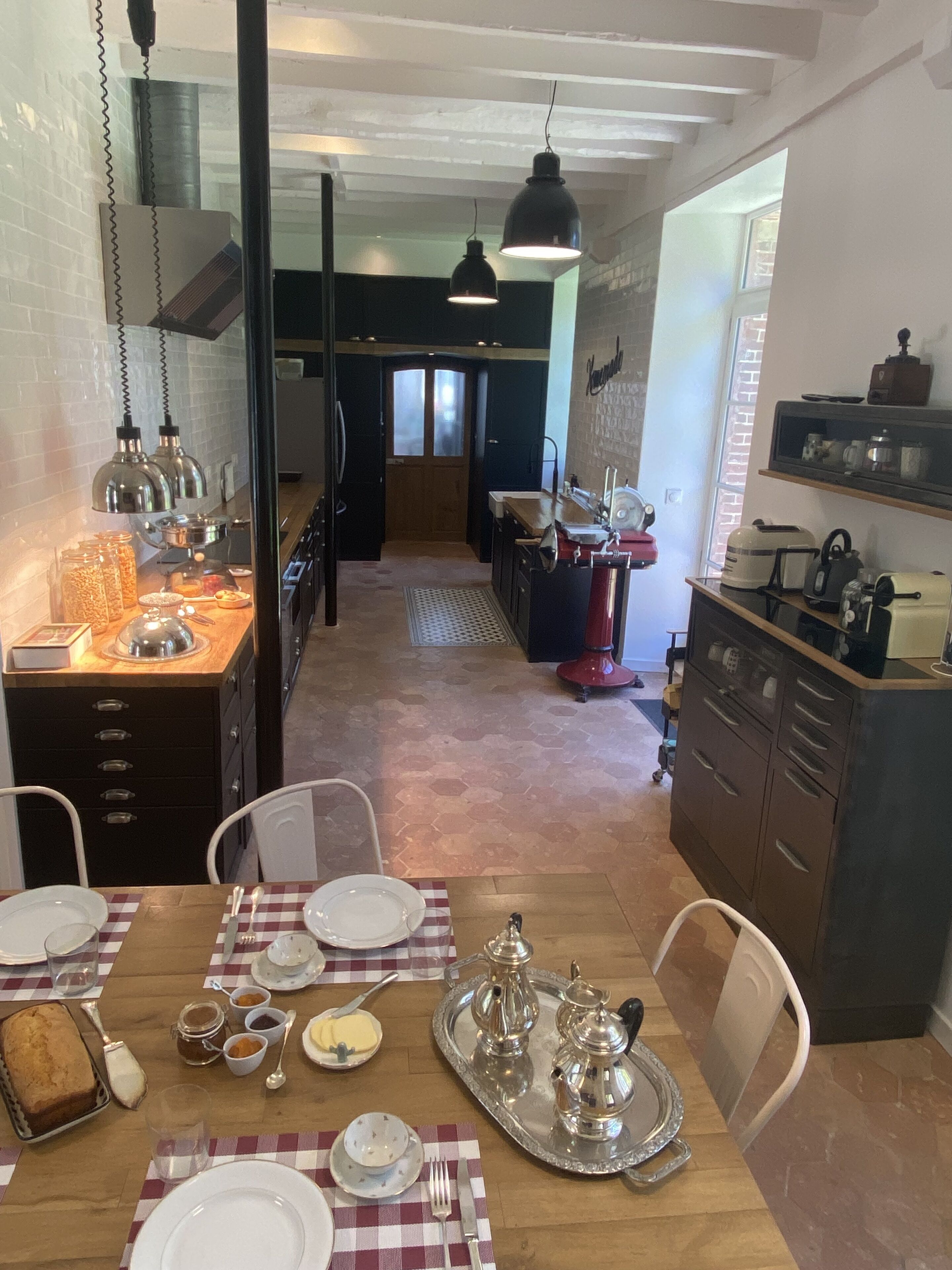 A dining area with a wooden table set for four, a kitchen in the background, and a view of the dining area through a glass door.