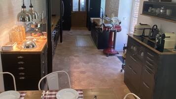 A dining area with a wooden table set for four, a kitchen in the background, and a view of the dining area through a glass door.