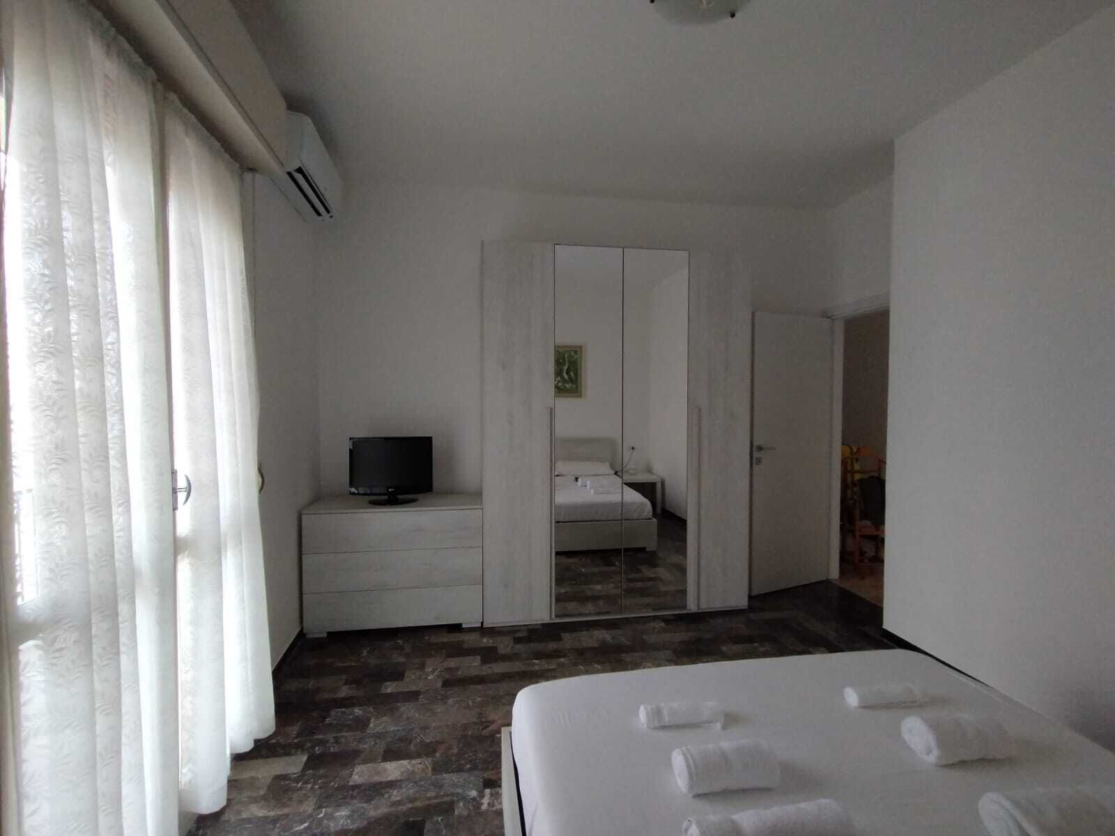 Ein Hotelzimmer mit einem Bett, einem Fernseher auf einer Kommode, einem Kleiderschrank und einem Spiegel, der den Raum wiederspiegelt.
