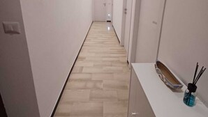 Un couloir étroit avec un plancher en bois, des murs blancs et une porte blanche au fond.