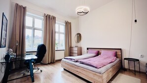 Ein modernes Schlafzimmer mit einem hölzernen Bett, einem Schreibtisch mit Stuhl, einer Pendelleuchte und Blick aus dem Fenster.