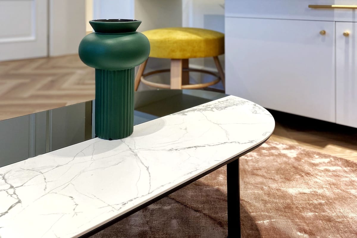 A modern kitchen with a marble countertop, a green vase, a yellow stool, and a white cabinet.