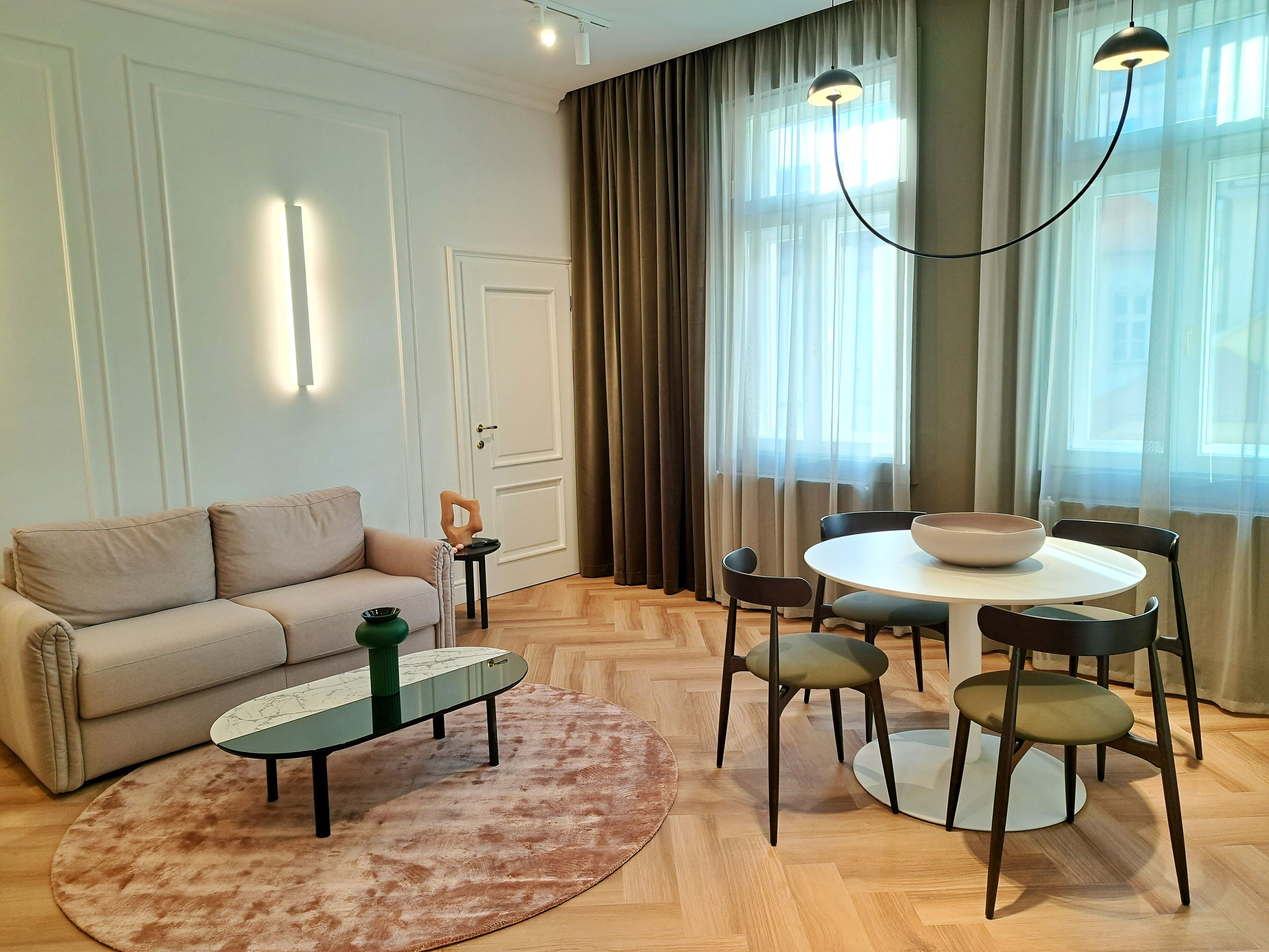 A modern living room with a sofa, a coffee table, a dining table with chairs, and a chandelier.
