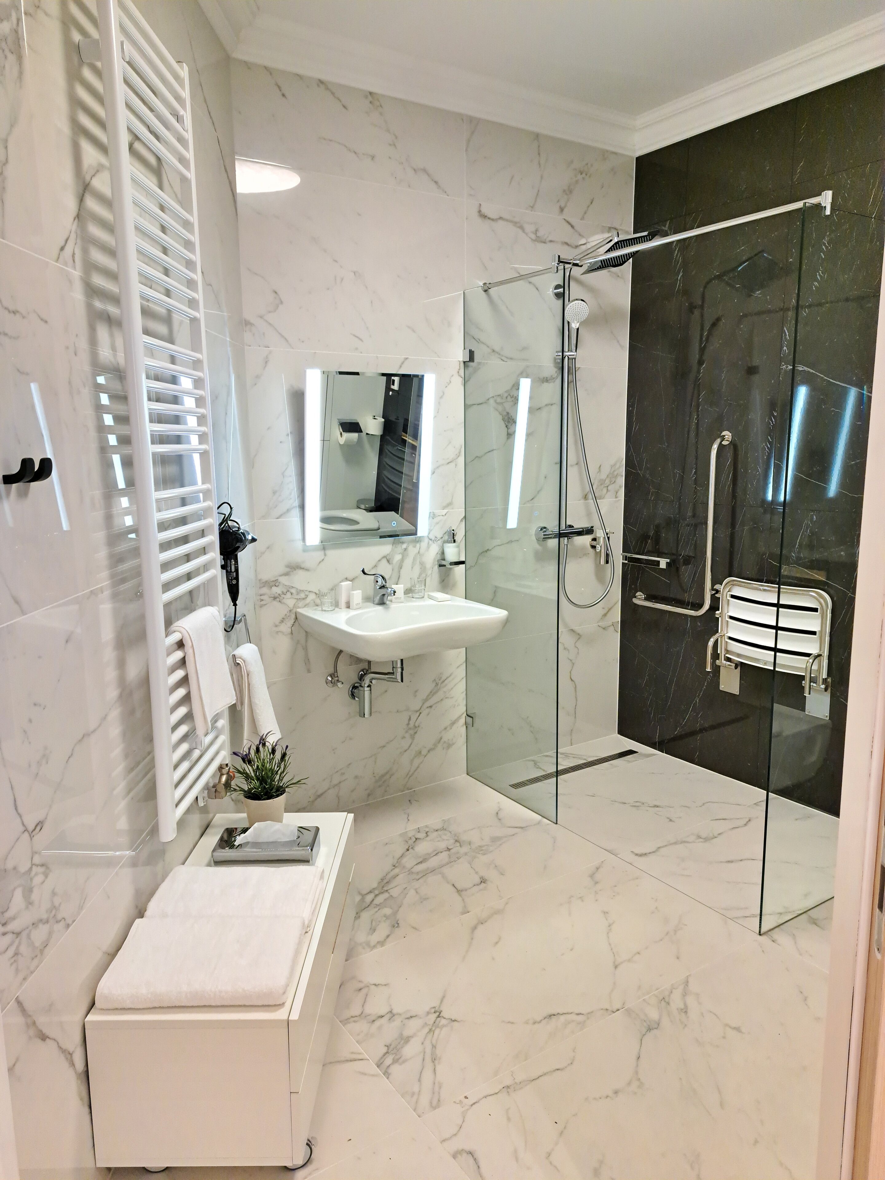 A modern bathroom with a glass-enclosed shower, a white sink, and a heated bench.