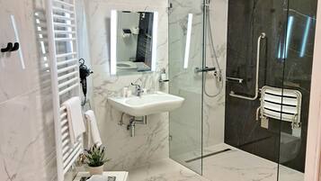 A modern bathroom with a glass-enclosed shower, a white sink, and a heated bench.