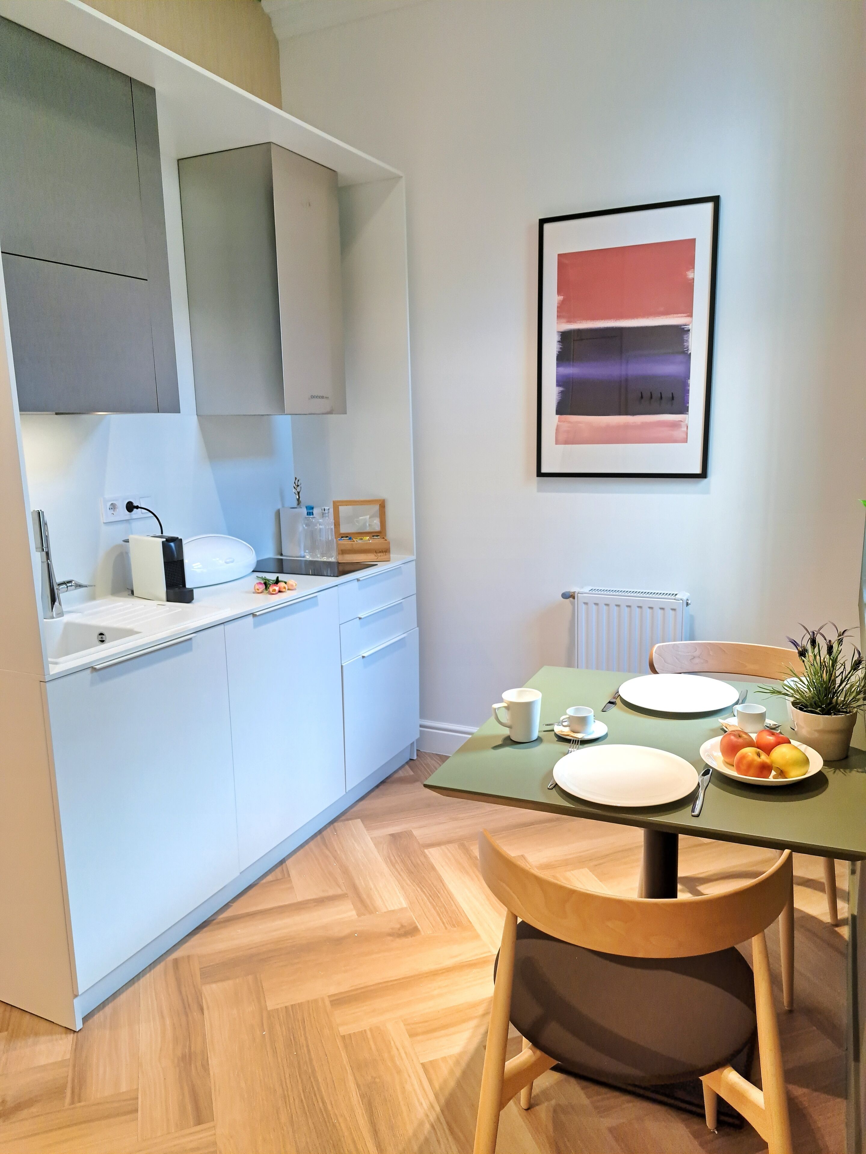 Una cocina moderna con armarios blancos, una mesa de comedor dispuesta con platos, tazas y un cuenco de fruta.