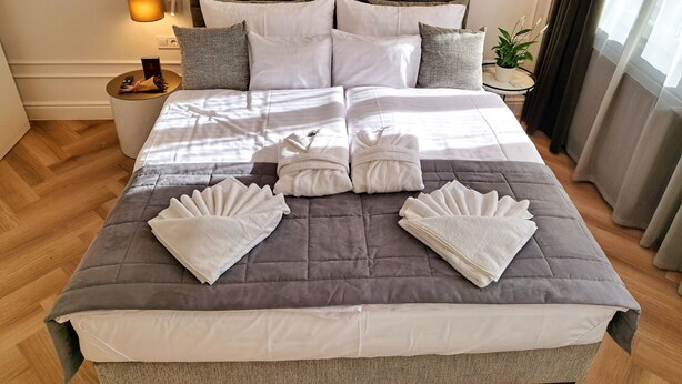 A neatly made bed with a grey quilt, white pillows, and a bedside table with a lamp and a small plant.